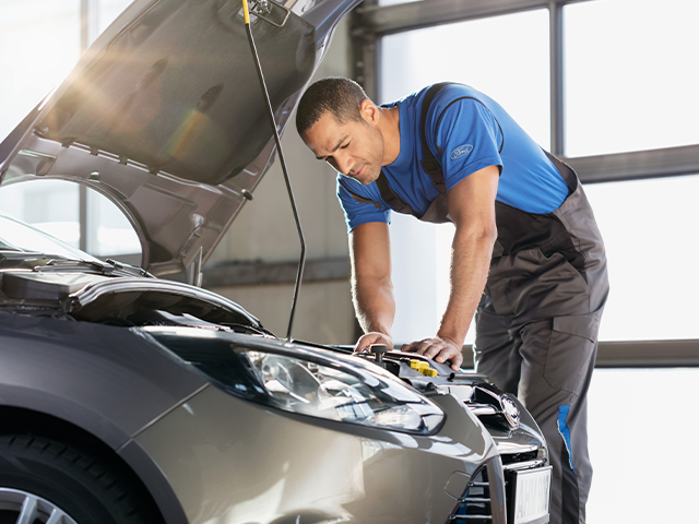 Ein Mechaniker arbeitet an einem Auto mit offenem Motorhaube in einer Werkstatt mit natürlichem Licht.