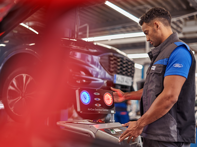 Ein Mechaniker überprüft eine Klimaanlage mit einem speziellen Gerät in einer Autowerkstatt.