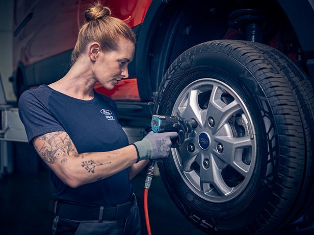 Eine Mechanikerin, die mit einem Schlagschrauber an einem Rad eines Fahrzeugs arbeitet.