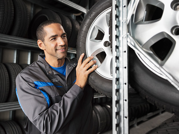 Ein Mechaniker lächelt, während er einen Reifen an einem Regal in einer Werkstatt betrachtet.