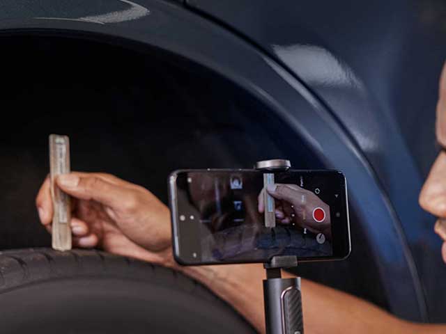 Eine Person misst die Profiltiefe eines Reifens mit einem Lineal, während sie mit einem Smartphone filmt.