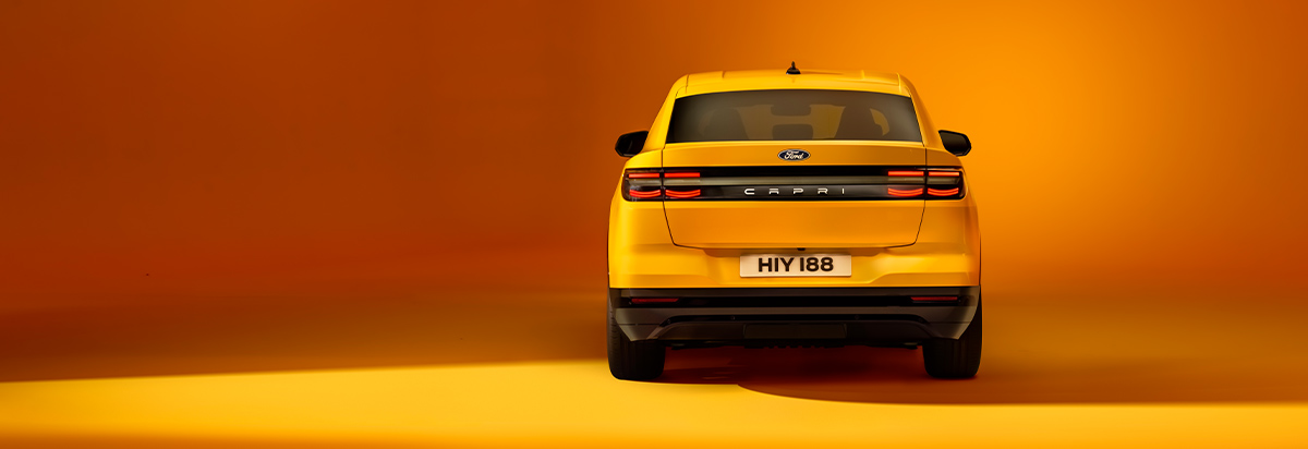 Rückansicht eines gelben Ford Fahrzeugs vor orangefarbener Hintergrundbeleuchtung.