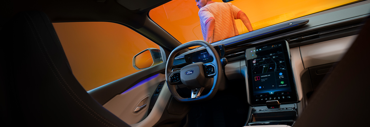 Innenraum eines modernen Ford-Fahrzeugs mit digitalem Display und einer Person im Hintergrund.