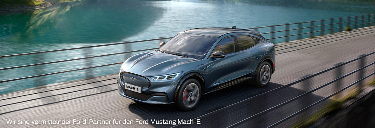 Der Ford Mustang Mach-E in Grau fährt über eine Brücke an einem klaren Gewässer entlang.