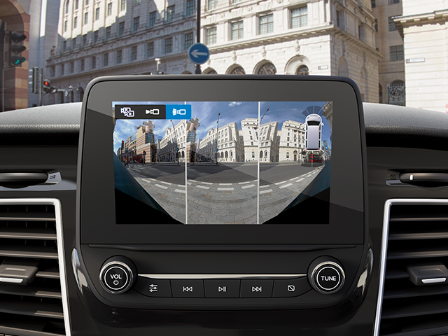 Display des Fahrzeugs mit Rückfahrkamera und Ansichten der Umgebung an einem Straßenkreuzung.