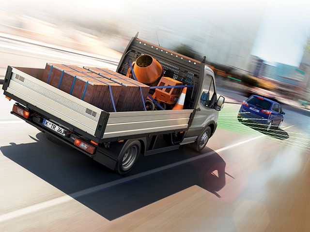 Ein Transporter mit Ladefläche, beladen mit Holz und Baumaschinen, fährt schnell auf einer Straße.