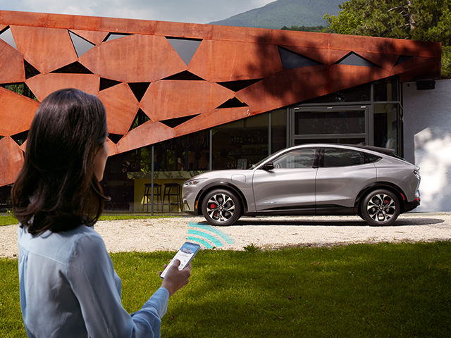 Eine Person nutzt ein Smartphone, um ein modernes Auto vor einem stilvollen Gebäude zu steuern.