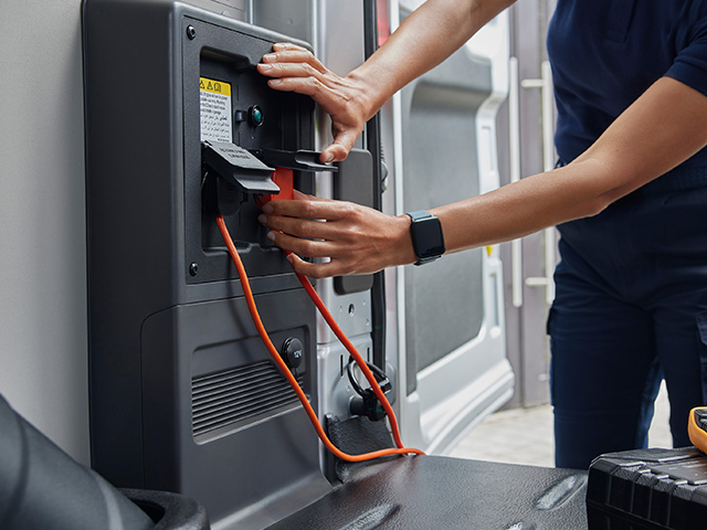 Eine Person schließt ein Kabel an eine elektrische Einheit in einem Fahrzeug an.