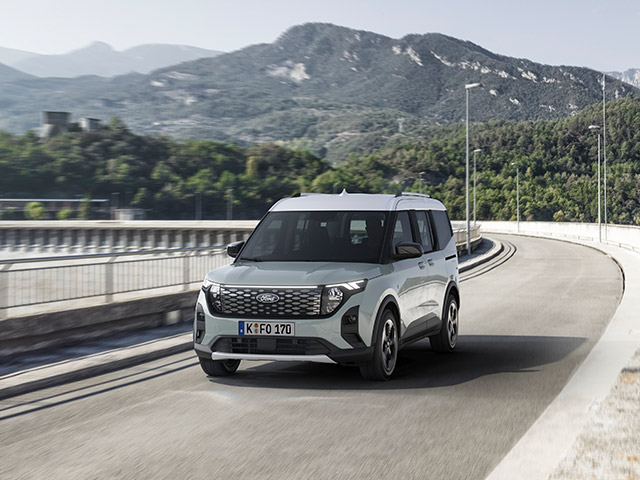 Ein grauer Ford-Fahrzeug fährt auf einer kurvenreichen Straße mit Bergen im Hintergrund.