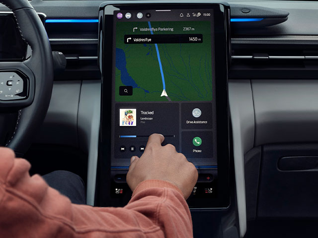 Eine Hand, die einen Touchscreen im Auto bedient, mit Navigationskarte und Mediensteuerung auf dem Display.