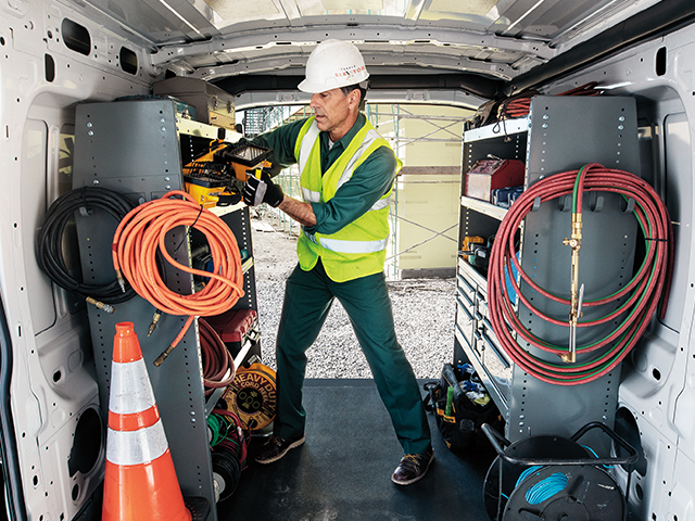 Ein Handwerker im Lieferwagen, der Werkzeuge organisiert, trägt einen Helm und Sicherheitskleidung.