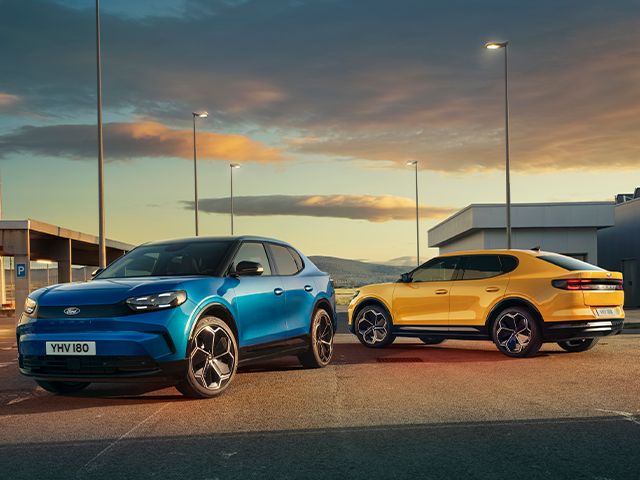 Zwei moderne Autos, ein blauer SUV und ein gelber Sportwagen, stehen auf einem Parkplatz bei Sonnenuntergang.