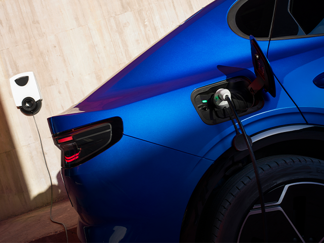 Ein blauer Elektroauto lädt an einer Ladestation mit einem Kabel, das an die Fahrzeugseite angeschlossen ist.