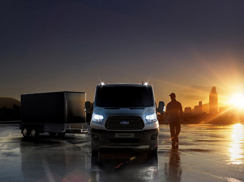 Ein Ford Transit Cabriolet steht vor einem Anhänger bei Sonnenuntergang auf einer nassen Straße.