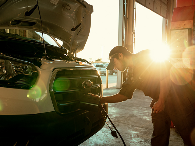 Mechaniker überprüft ein Auto im Sonnenuntergang mit offenem Motorraum in einer Werkstatt.