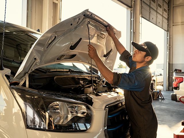 Mechaniker überprüft Motorhaube eines Fahrzeugs in einer Werkstatt, um Reparaturen durchzuführen.