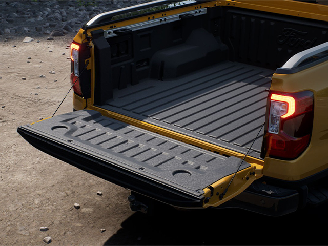 Offene Ladefläche eines gelben Pickups mit robustem Bodenbelag, auf einem unebenen Untergrund.