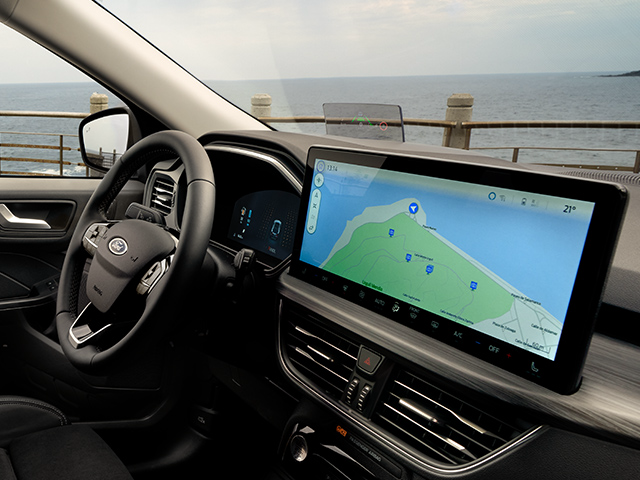 Innenansicht eines Fahrzeugs mit einem modernen Navigationsdisplay und Blick auf die Küste im Hintergrund.