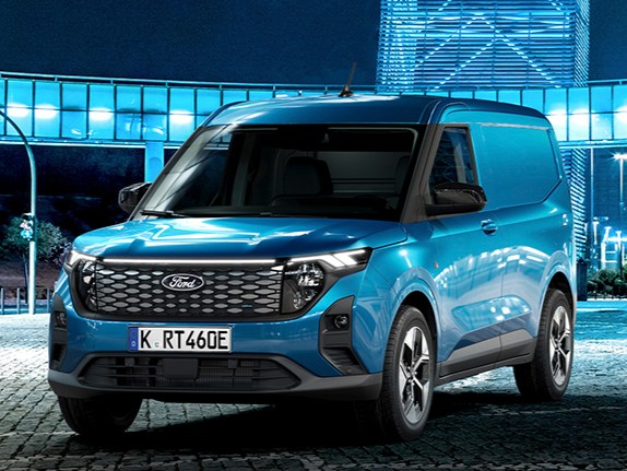 Blauer Ford Transporter vor moderner Architektur bei Nacht beleuchtet.