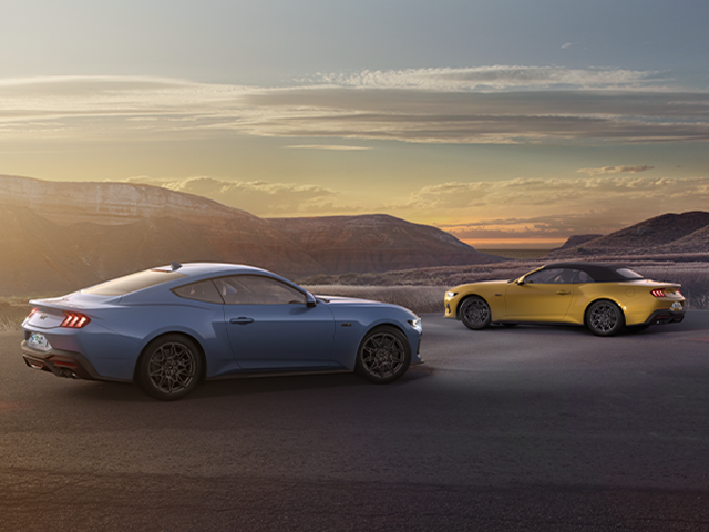 Zwei sportliche Autos, ein blaues Coupé und ein gelbes Cabriolet, stehen bei Sonnenuntergang auf einer Straße.