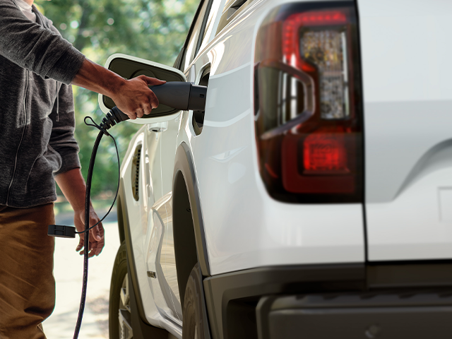 Ein Mann lädt ein Elektrofahrzeug mit einem Ladekabel an einer Ladesäule auf.