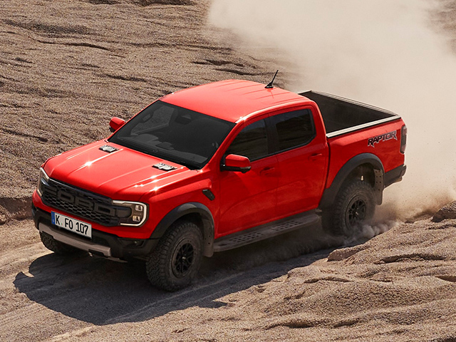 Ein roter Pickup-Truck fährt durch Sand, mit Staubwolken im Hintergrund.