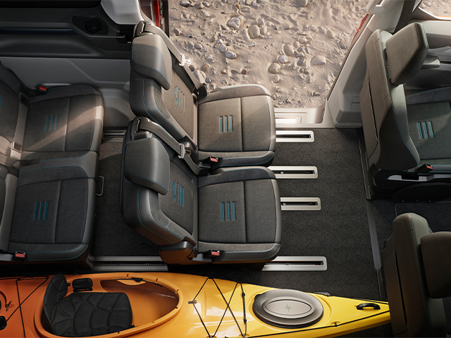 Innenansicht eines Fahrzeugs mit drei Sitzen und einem gelben Kajak auf dem Boden.