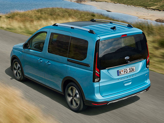 Blauer Ford Tourneo fährt auf einer Landstraße, im Hintergrund Wiese und Wasser.